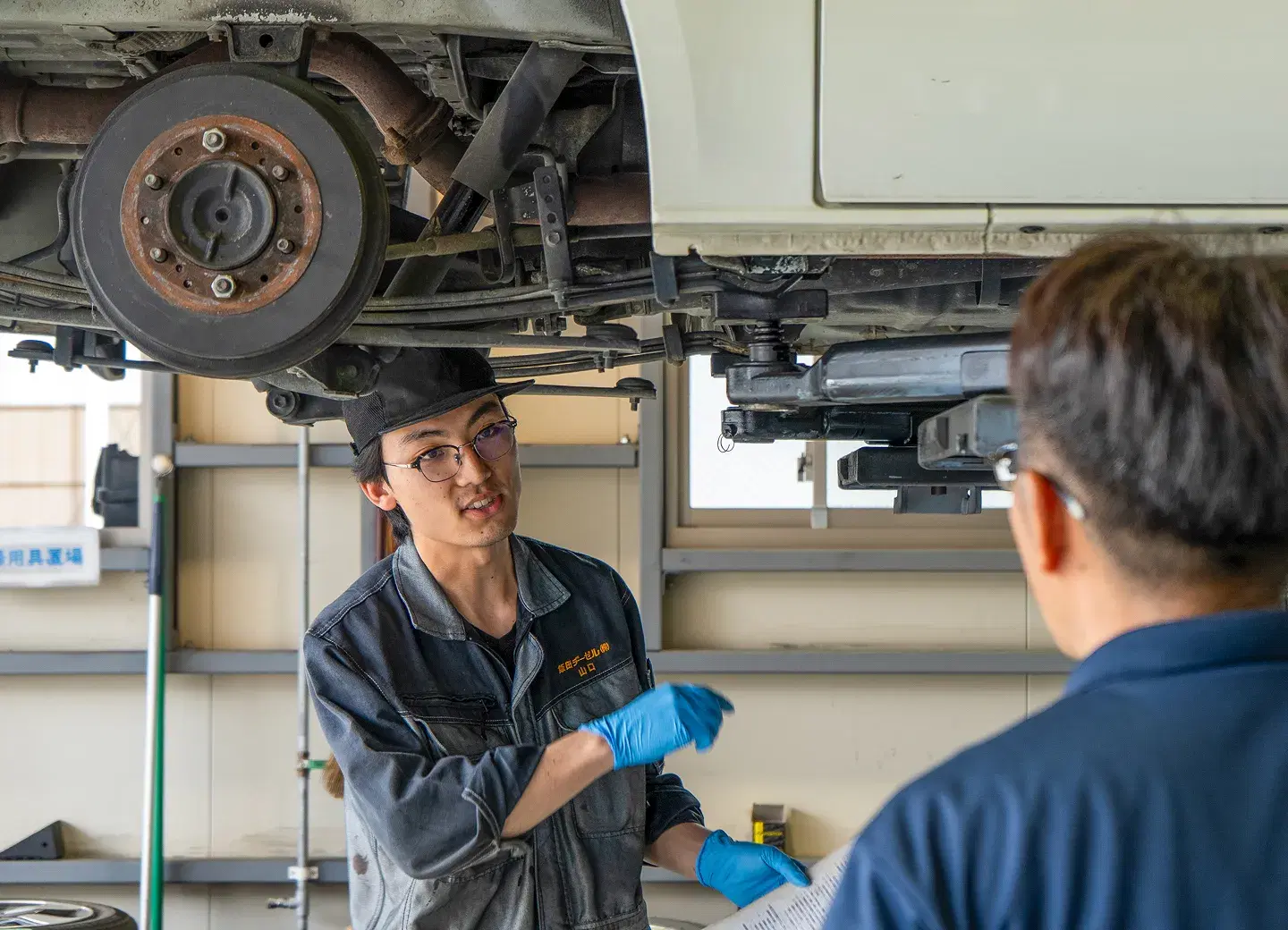 リフトで上げた車の足回りを確認する整備士